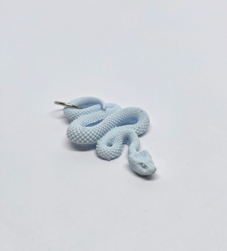 Ręcznie wykonana zawieszka z żywicy. Kształt zwiniętego w zygzak węża. Wąż jest 3D i posiada szczegóły, takie jak zarys oczu i łuski. Zawieszka w kolorze jasno-błękitnym. Kółeczko montażowe w kolorze srebrnym do zaczepienia zawieszki.