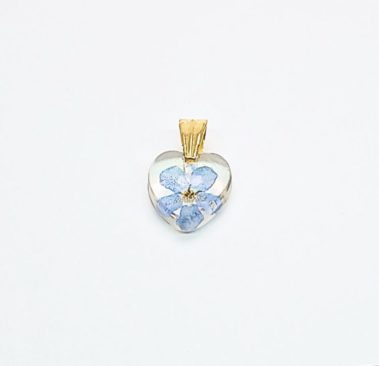 Wisiorek mini serduszko z przejrzystej żywicy, z zatopionym prawdziwym kwiatem niebieskiej niezapominajki. Krawatka w kolorze złotym z pionowymi żłobieniami. Wisiorek ma 1,5 cm długości z krawatką.